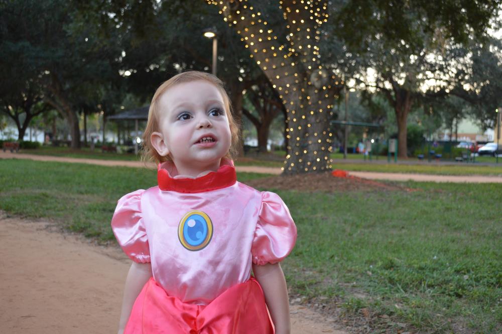 Young girl in pink princess outfit with tree wrapped in lights in background